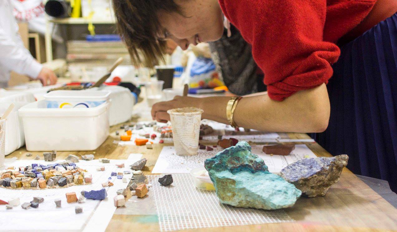 A studio member selecting raw turquoise and azurite stone pieces for mosaic work